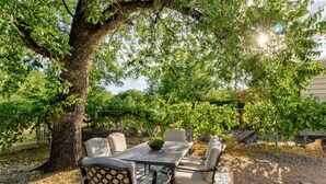 Eine Terrasse im Freien mit Tisch und Stühlen, umgeben von Bäumen und einem Zaun.