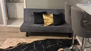 A modern living room with a grey sofa, a black and gold patterned rug, and a dining area with a white table and grey chairs. - The Jones Suites (Freeport)