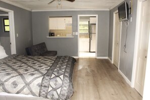 Relax in this inviting bedroom with a large bed and ceiling fan, featuring a television and a doorway to a kitchen area.