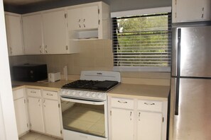 Kitchen features a gas stove, oven, microwave, and window with blinds.