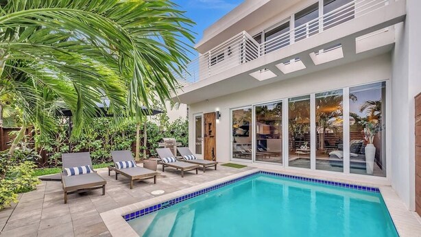 Ett modernt hus med en swimmingpool, solstolar och en stor glasdörr som leder ut till en uteplats.