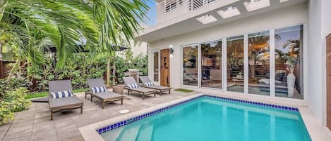 Uma casa moderna com piscina, espreguiçadeiras e uma grande porta de vidro que dá para um terraço.