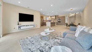 Ett modernt vardagsrum med en platt-TV, en soffa, ett soffbord och en matplats i bakgrunden.