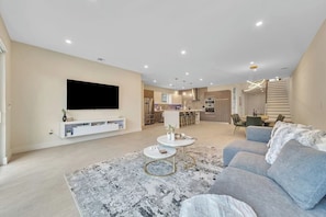 A modern living room with a flat-screen TV, a sofa, a coffee table, and a dining area in the background.