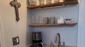 Et køkken med en granitbordplade, stålvask, kaffemaskine og et kors på væggen.