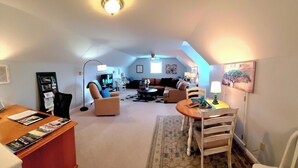 Et hyggeligt loftsrum med sofa, stole, sofabord og et fjernsyn.