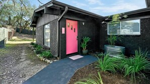 Ein modernes Haus mit einer auffälligen rosafarbenen Tür, einer Ziegel Fassade und einem kleinen Garten mit Blumentöpfen.