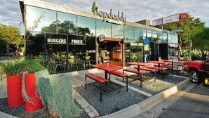 Ein Restaurant mit Außenbereich, Glasfassade und Schildern für Burger und Pommes.