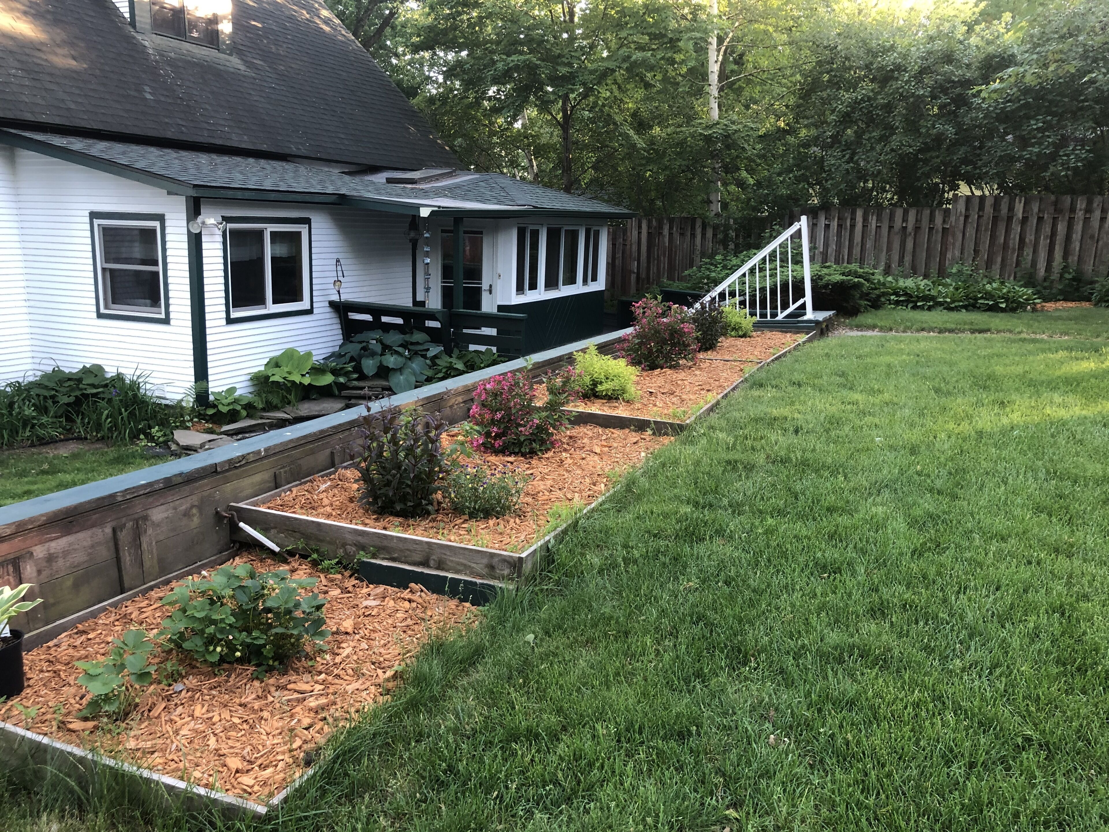 Een huis met voortuin, een houten terras en een houten omheining.