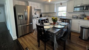 A modern kitchen with stainless steel appliances, white cabinets, and a dining area set for four. - 4br & 2ba Ranch style house w/ huge backyard! (PORTSMOUTH)