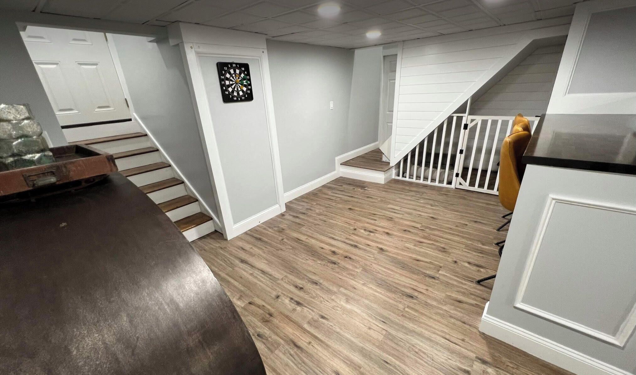 Una habitación amplia con suelo de madera, paredes blancas y una escalera que sube a otro nivel.