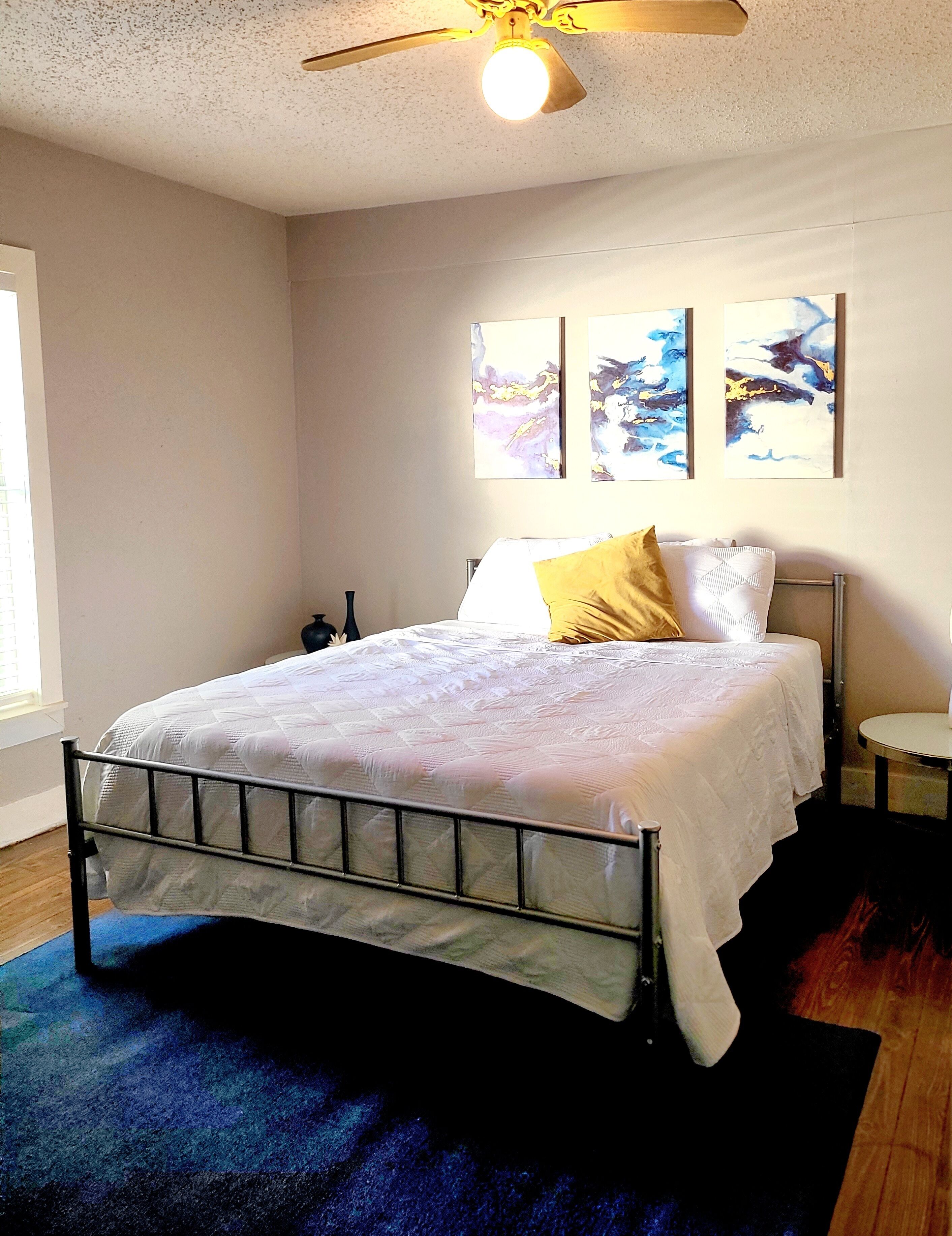 Un dormitorio con cama, ventilador de techo y decoración abstracta en la pared.