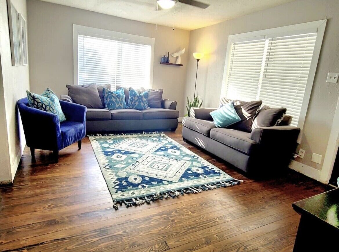 A living room with a blue armchair, a grey sofa, and a patterned rug.