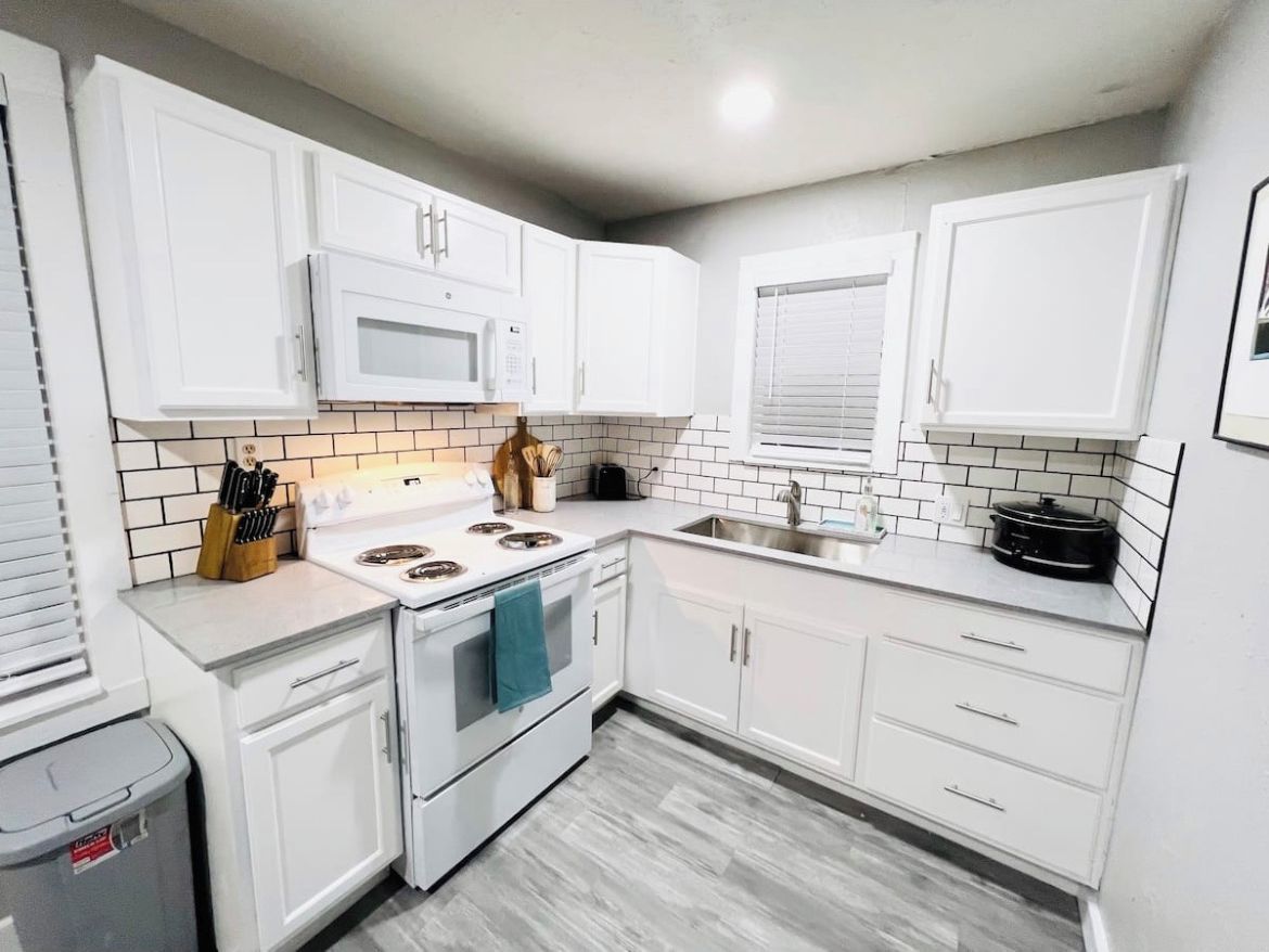 A modern kitchen with white cabinets, a microwave, stove, and a sink.