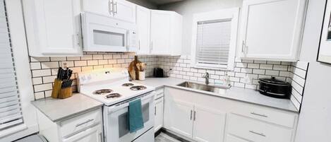A modern kitchen with white cabinets, a microwave, stove, and a sink.