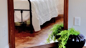 Une chambre avec un grand miroir, un lit recouvert d’une literie blanche et une plante en pot posée sur le sol.