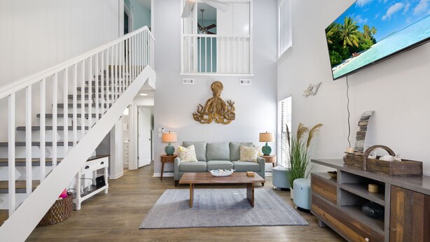 A living room with a staircase, a sofa, a coffee table, and a TV on the wall. - Vacation at the most beautiful beaches (Panama City Beach)