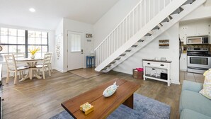 A spacious living room with a wooden coffee table, a dining area with a white table and chairs, a kitchen with white cabinets and a stove, and a white staircase. - Vacation at the most beautiful beaches (Panama City Beach)