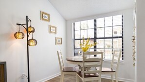 A dining area with a round table, white chairs, a floor lamp, and a window with blinds. - Vacation at the most beautiful beaches (Panama City Beach)