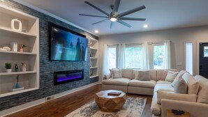 A modern living room with a flat-screen TV, wooden flooring, a ceiling fan, and a beige sofa. - Five75 Lux ATL King Bed & Game Room Downtown (Atlanta)