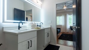 A modern bathroom with a large mirror, white cabinetry, and a black rug. - Five75 Lux ATL King Bed & Game Room Downtown (Atlanta)