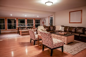 Una sala de estar amplia con un sofá de cuero marrón, dos sillones estampados, una mesa de centro y un comedor con una mesa y sillas de madera.