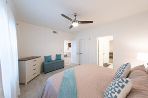 Un dormitorio con cama, cómoda, banca, ventilador de techo y puerta que da a un baño.
