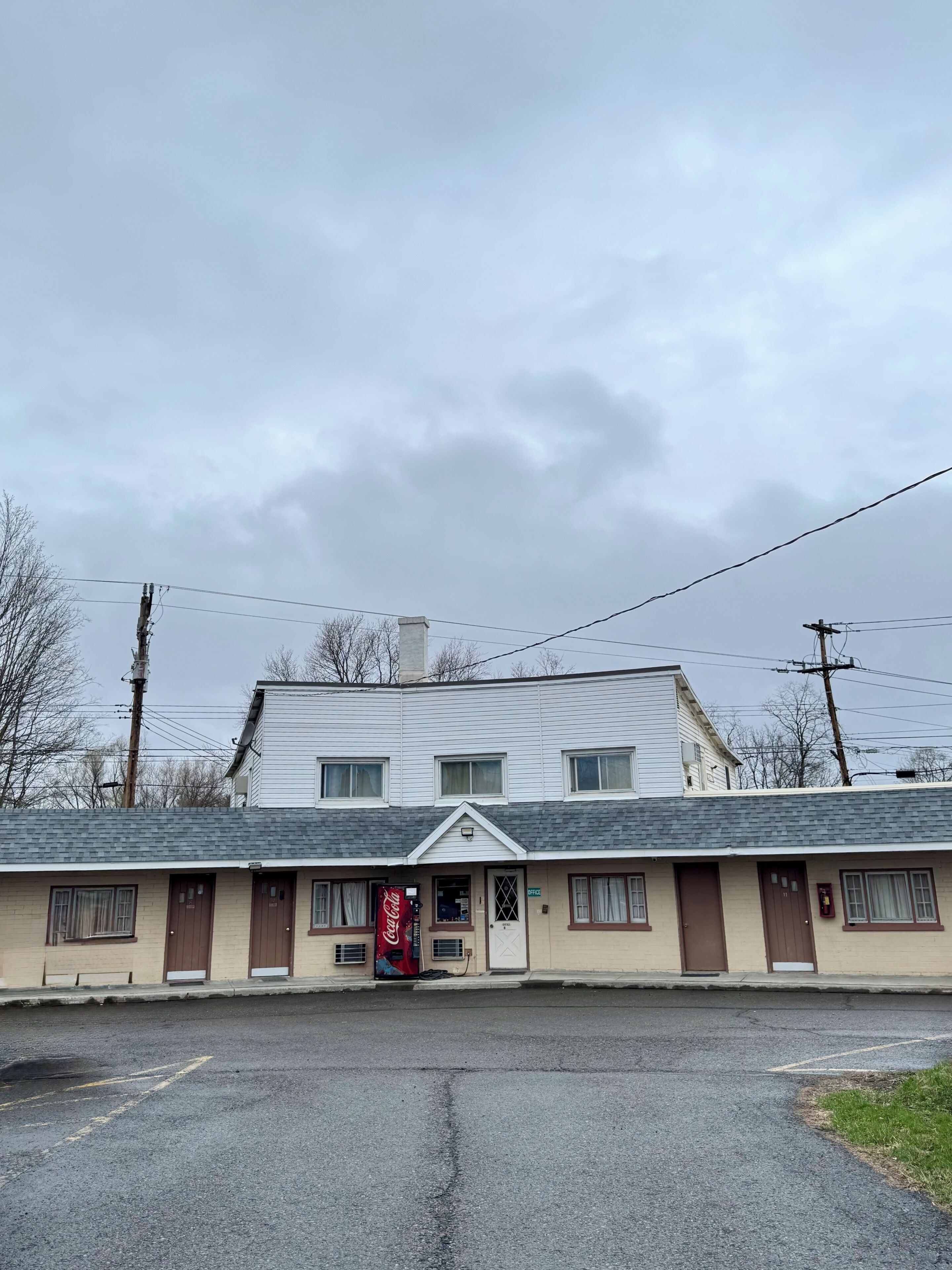 Un motel con entrada central, un letrero de Coca-Cola y un estacionamiento pequeño.