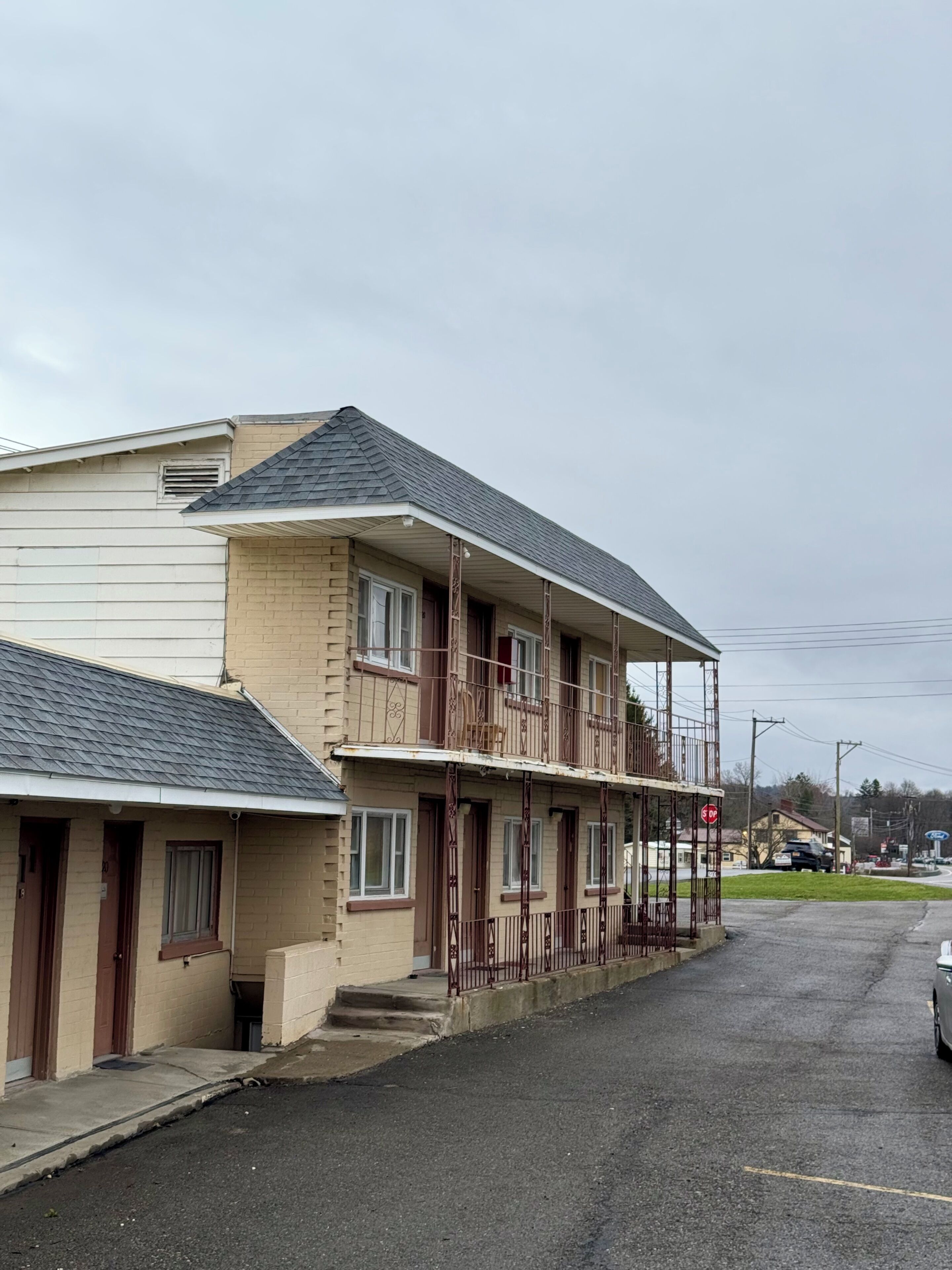 Un motel à deux étages doté d’un balcon au deuxième étage, d’un espace de stationnement couvert et donnant sur la rue.