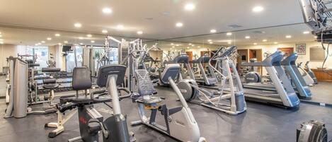 Un gimnasio con diferentes máquinas de ejercicio, espejos y un ventilador de techo.