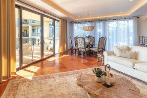 A spacious living area with a large sliding glass door leading to an outdoor balcony, a dining table with chairs, and a white sofa.