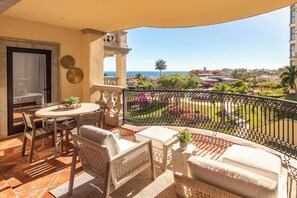 A balcony with outdoor furniture, a view of the sea, and a garden.
