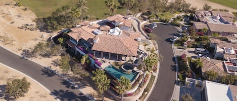 A residential area with a swimming pool, multiple houses with tiled roofs, and a golf course in the background.