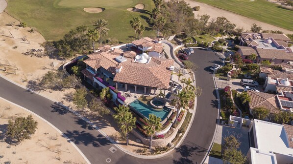 A residential area with a swimming pool, multiple houses with tiled roofs, and a golf course in the background.
