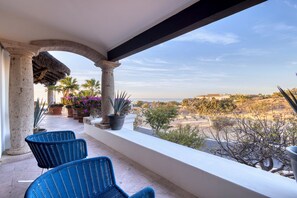 A balcony with two blue chairs, a thatched roof, and a view of a desert landscape.