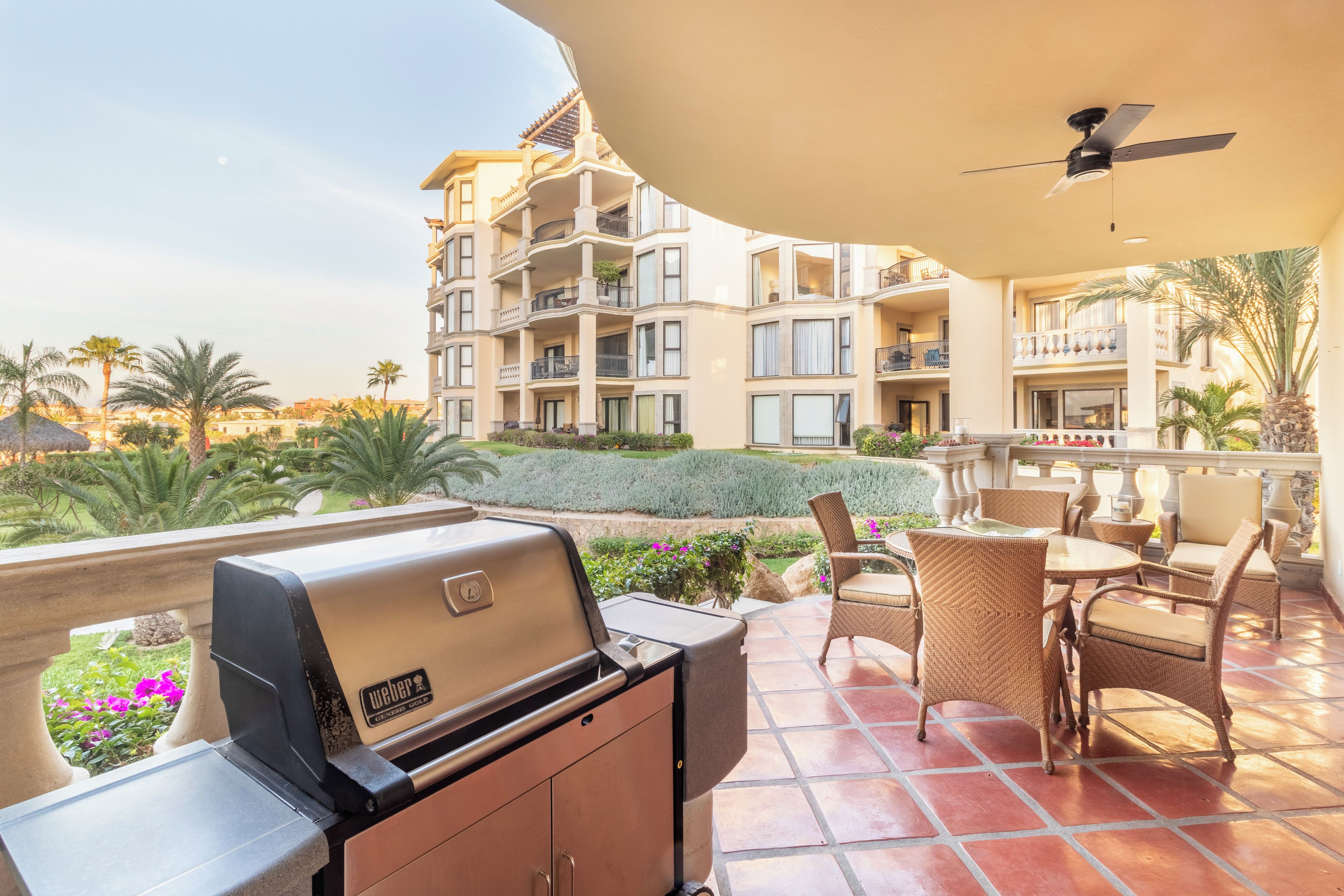 A patio with a Weber Genesis Gold grill, outdoor furniture, and a view of a multi-story building with balconies.