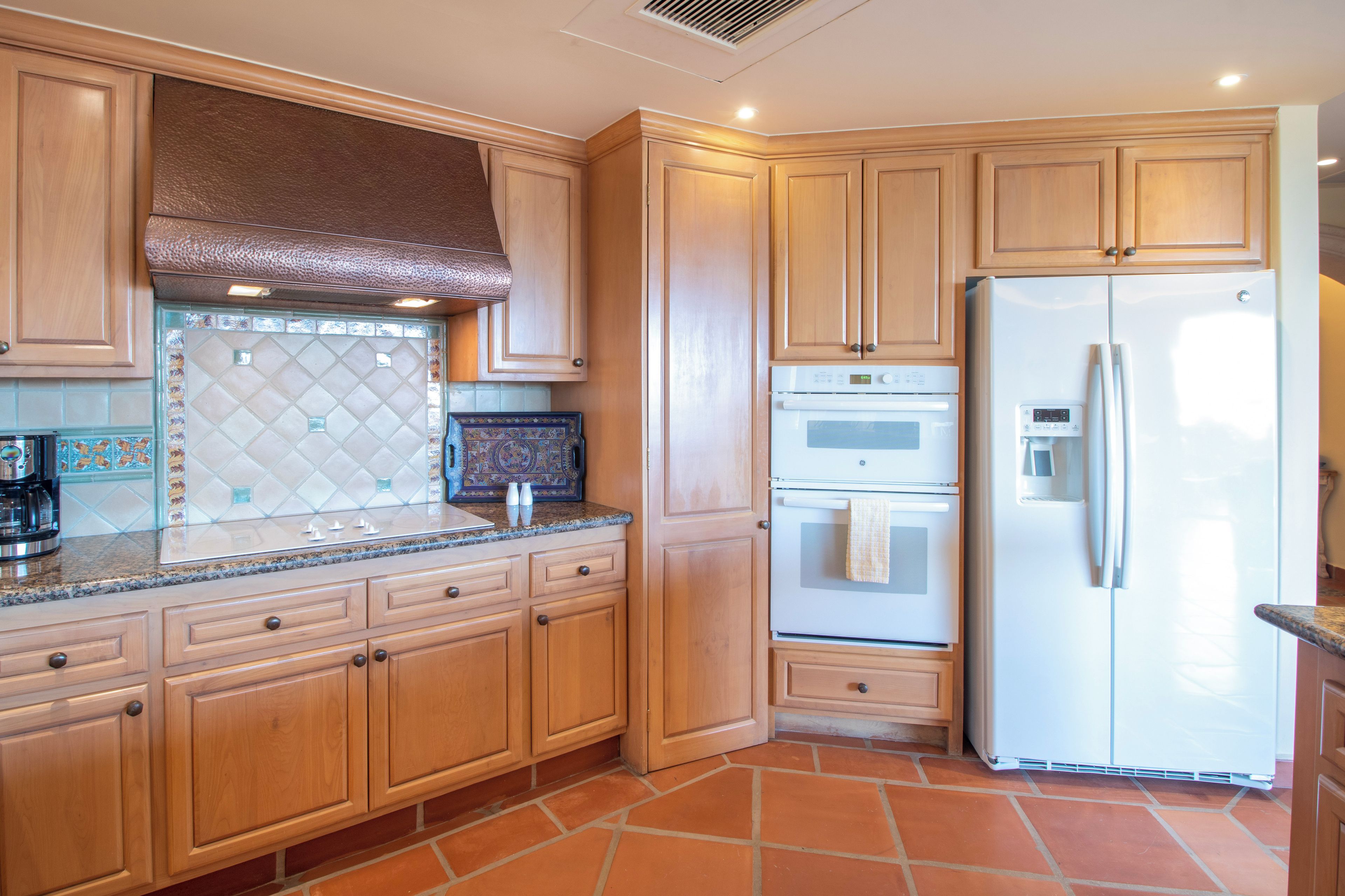 A kitchen with wooden cabinets, a stainless steel range hood, a built-in oven, and a white refrigerator.