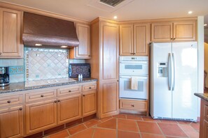 Eine Küche mit Holzausstattung, einer Edelstahl-Dunstabzugshaube, einem eingebauten Backofen und einem weißen Kühlschrank.