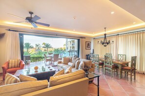 A spacious living area with a sofa set, a dining table with chairs, a ceiling fan, and a view of the outdoors.