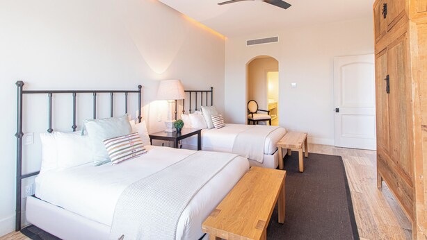 Ein Schlafzimmer mit zwei Betten, einem Deckenventilator, einer Holzbank und einer Tür.