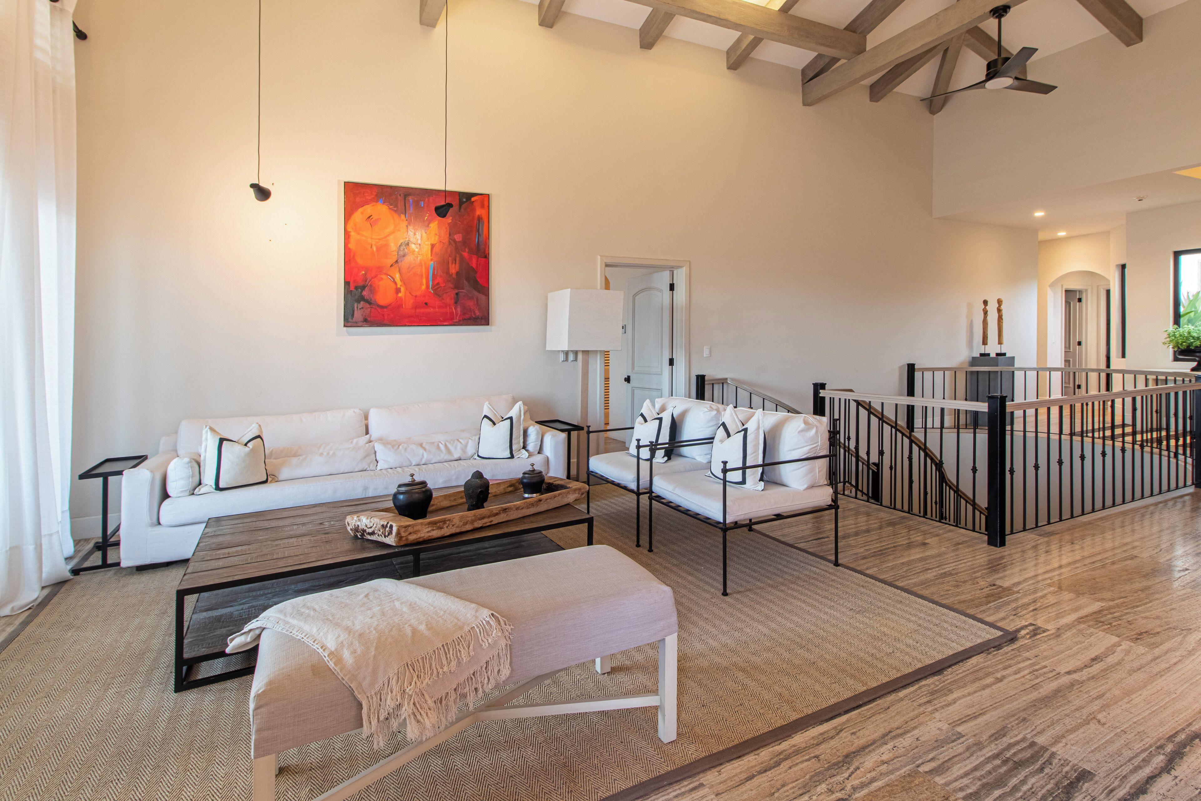 Ein geräumiges Wohnzimmer mit einem weißen Sofa, einem Couchtisch und einer Bank. An der Wand hängt ein Gemälde, und eine Treppe führt auf eine erhöhte Ebene.