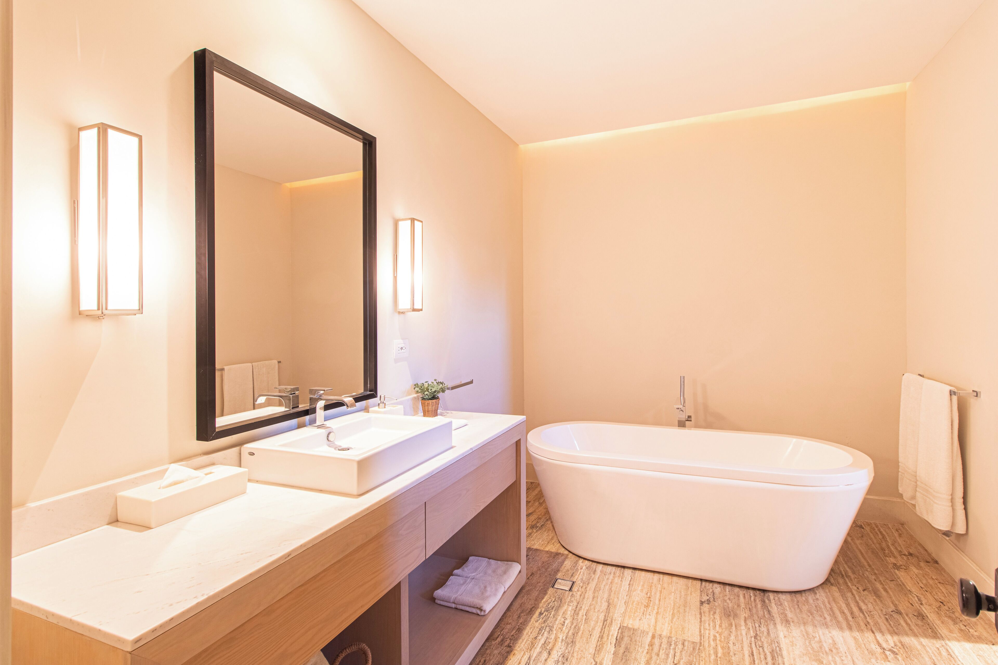 Een moderne badkamer met een vrijstaand bad, een grote spiegel en een wastafelmeubel met een wastafel en handdoekhouder.