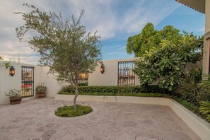 A courtyard with a tree, potted plants, and a building with a white facade and decorative iron gates. - Villa Perdiz, Puerta del Sol | 4 Bed, 4 Bath (Cabo San Lucas)