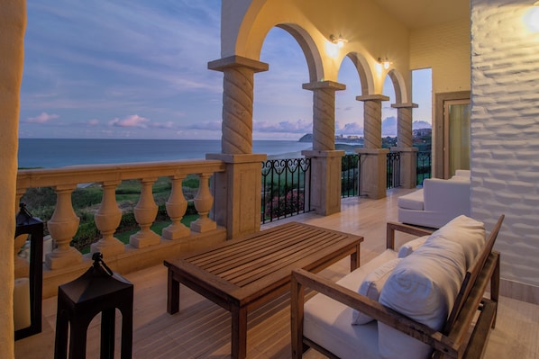 A balcony with a wooden table and sofa, a view of the sea, and a stone balustrade.
