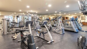 Ein Fitnessstudio mit verschiedenen Trainingsgeräten, einer Spiegelwand und einer Decke mit eingelassener Beleuchtung.