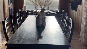 Ein Esszimmer mit großem Holztisch, schwarzen Stühlen, einer gewebten Pendelleuchte und Blick auf die Landschaft durch große Fenster.