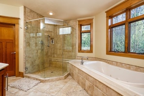 A bathroom with a glass-enclosed shower, a large bathtub, and a window with a view of trees.