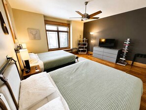 Ein Hotelzimmer mit zwei Betten, einem Deckenventilator, einem Fernseher, einem Bücherregal und einem Fenster.