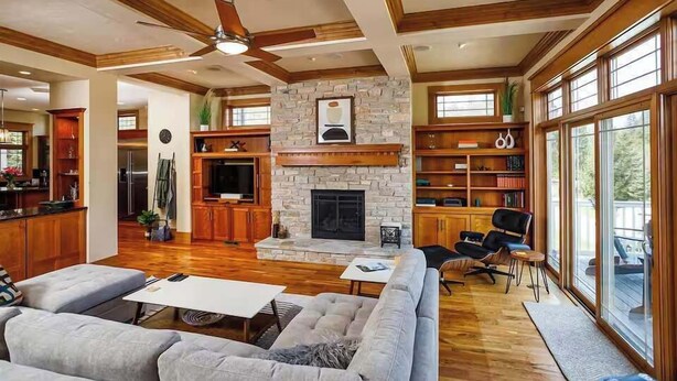 A spacious living room with a fireplace, wooden ceiling beams, and large windows.
