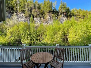 Eine Holzterrasse mit weißer Brüstung, einem runden Tisch und zwei Holzstühlen.